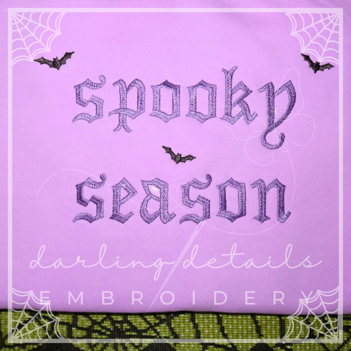 A square embroidery design preview on a lavender fabric background with stitched gothic text reading 'spooky season,' white script text reading 'darling details,' and 'EMBROIDERY' at the bottom. Decorative spiderwebs and three black bats appear around the design.